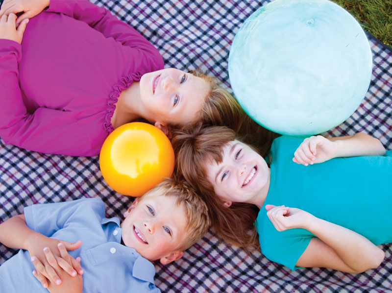 Three young children laying on their backs on a plaid blanket all are smiling