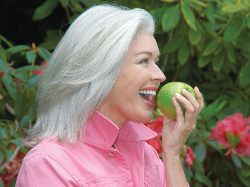 Woman outdoors getting ready to bite into a green apple and smiling
